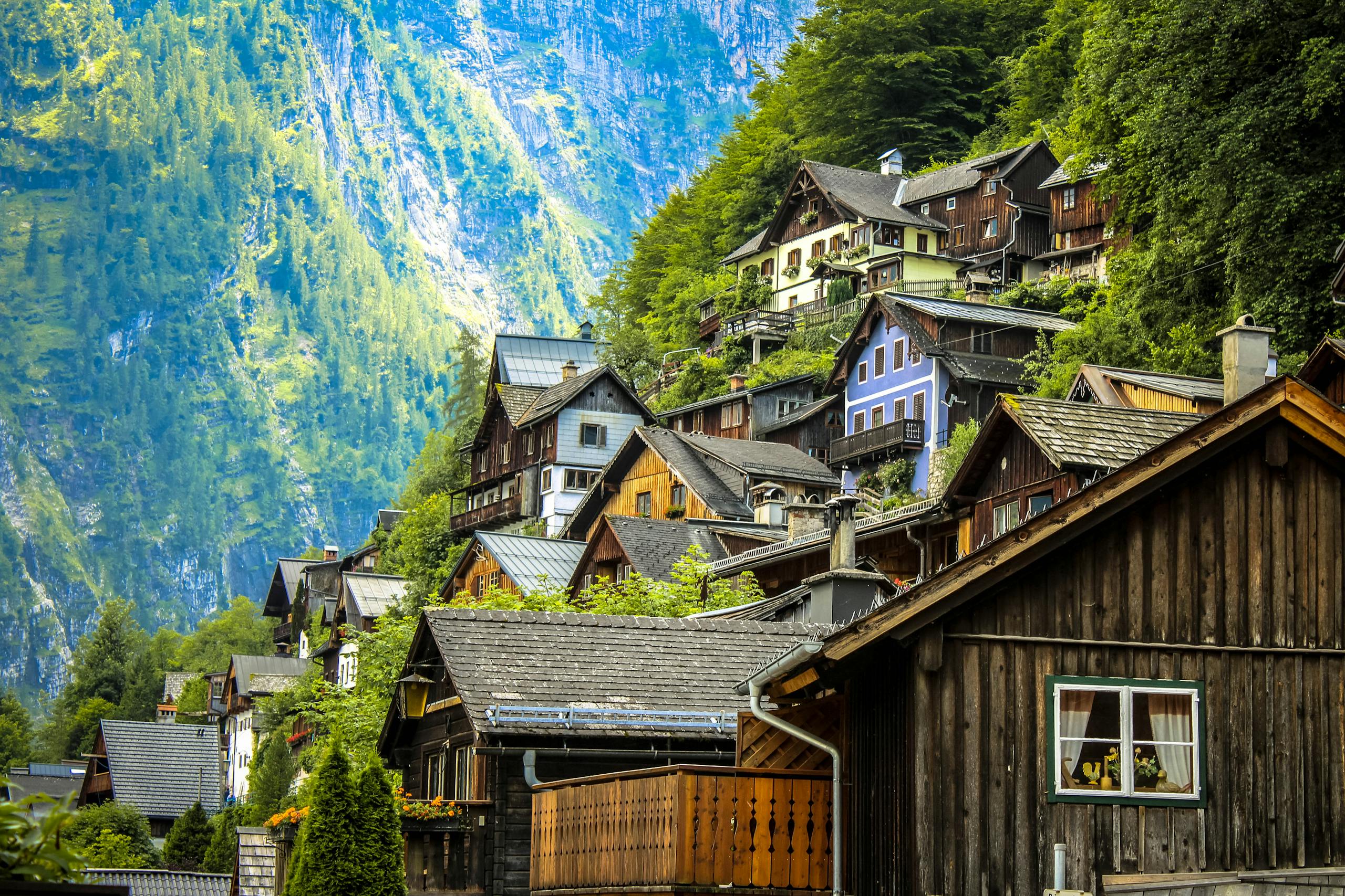 Charming wooden houses on a lush mountainside in Hallstatt, Austria under bright daylight.