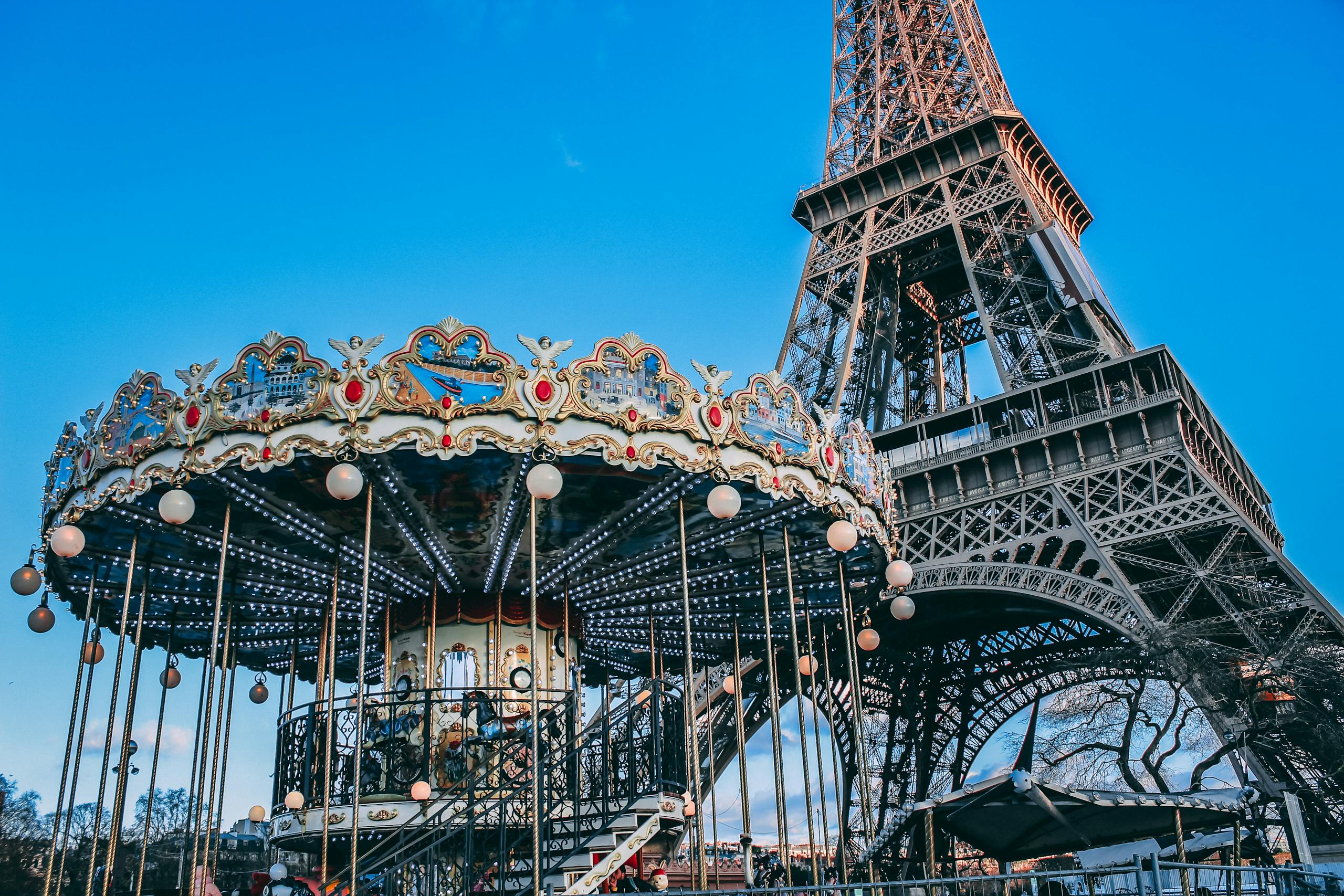 Eiffel Tower with a classic carousel in foreground on a bright day in Paris, France.