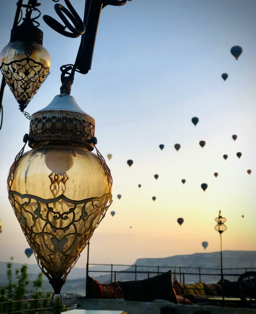 Hot air balloons float over Göreme, Turkey at dawn, with decorative lamps in the foreground.