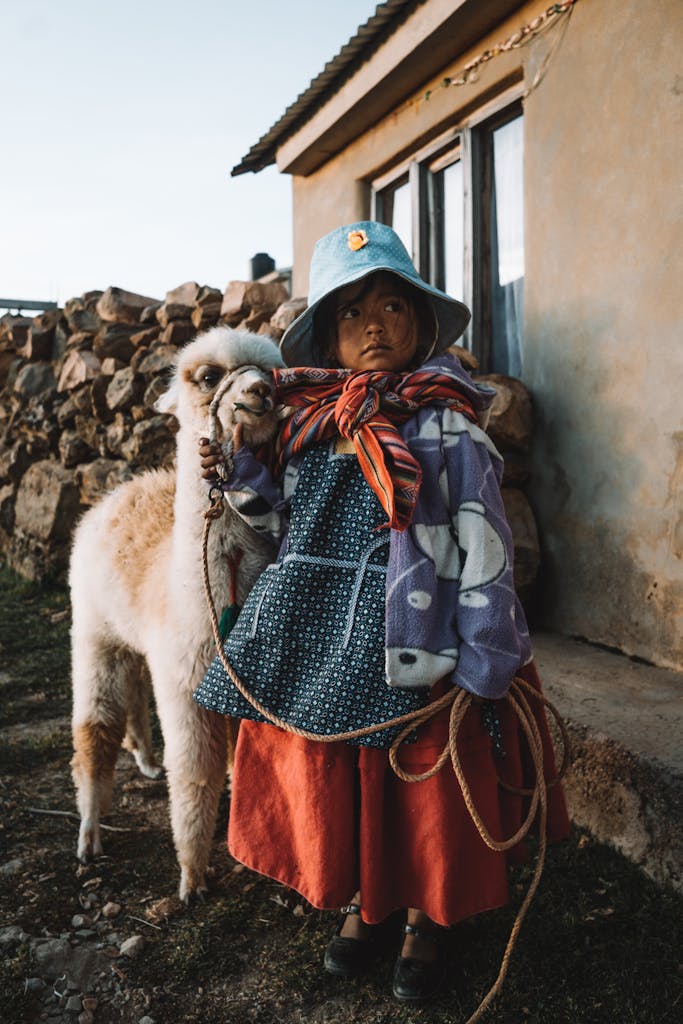 Young girl in traditional clothing with a llama, captured outdoors in a rural setting.